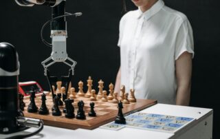 AI robotic arm moving chess pieces on a board while a human observes, symbolizing AI strategy, automation, and human oversight in decision-making and workforce evolution.